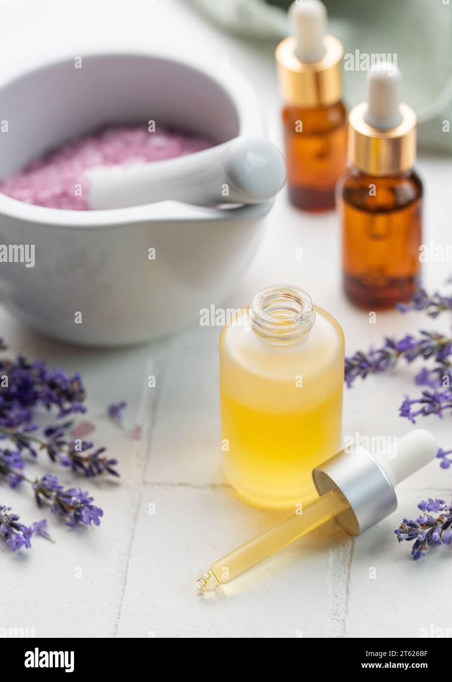 Vasca idromassaggio con lavanda. Sale di lavanda, olio essenziale naturale e lavanda fresca su fondo di piastrelle bianche. Foto Stock