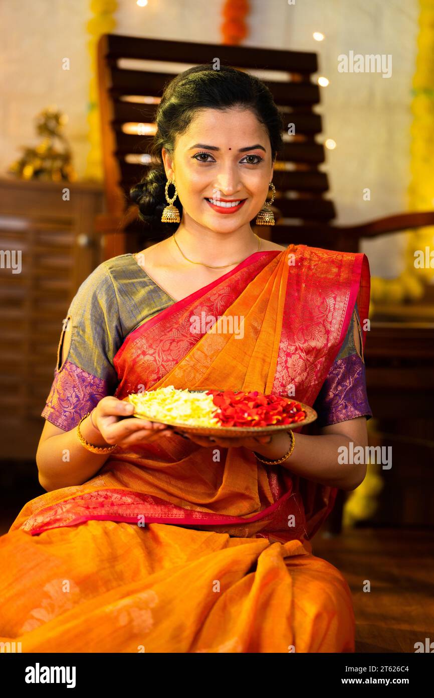 Foto verticale di una ragazza indiana felice che tiene un piatto di fiori per la celebrazione diwali guardando la macchina fotografica a casa - concetto di tradizionale indiana, cerimonia Foto Stock