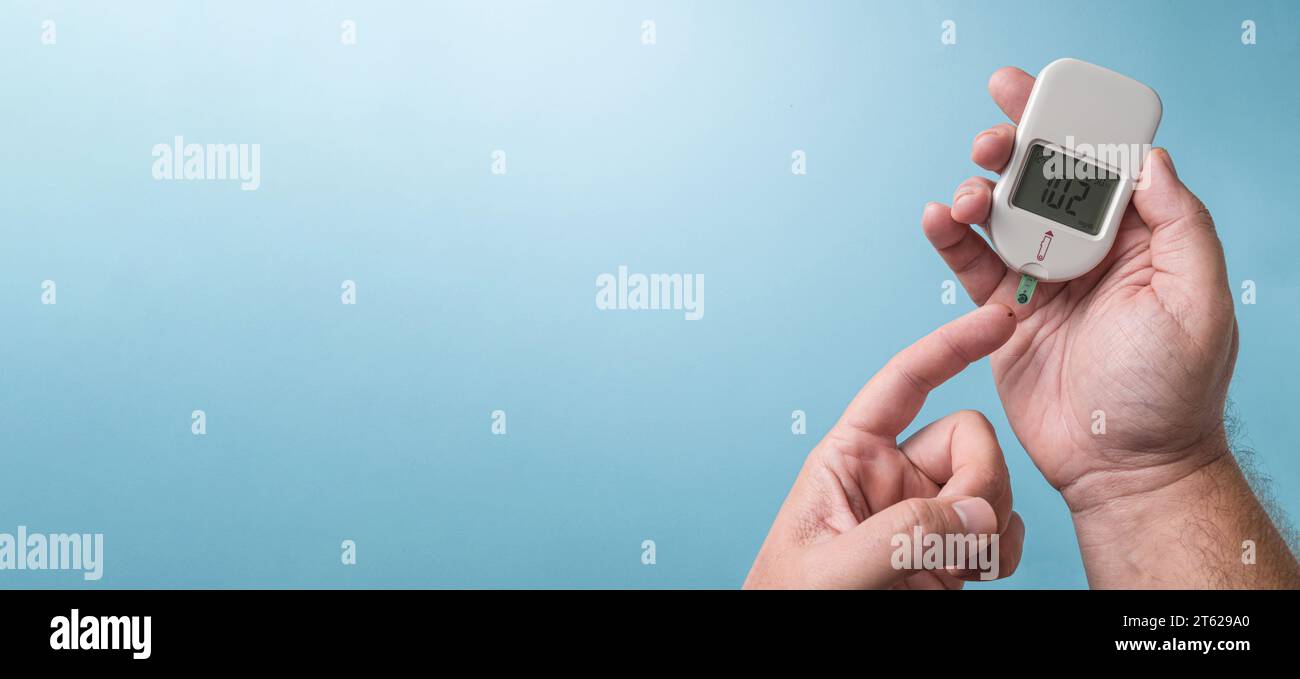 Uomo che misura il livello di zucchero nel sangue con un glucometro. Concetto di diabete su sfondo blu Foto Stock