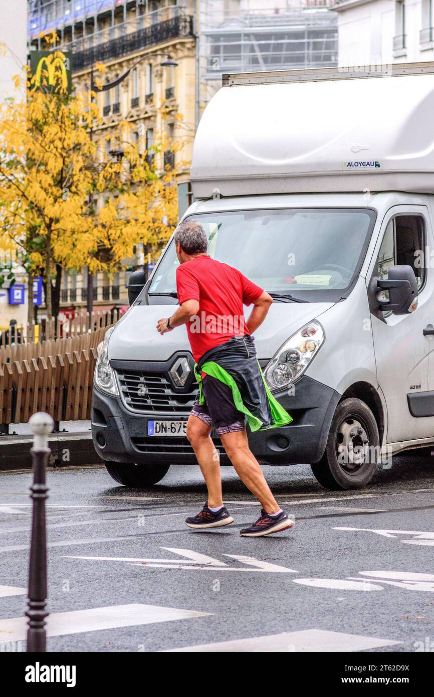 Jogger anziano che corre di fronte al traffico nel centro della città - Parigi 20, Francia. Foto Stock