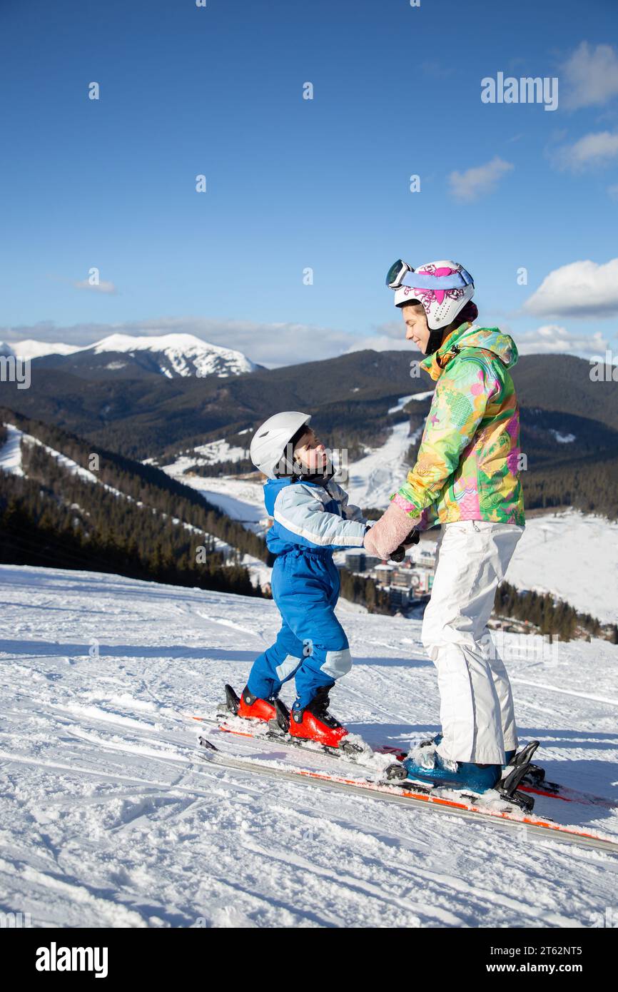 bambino e adolescente in età prescolare si trovano su una pista di montagna con gli sci che si tengono per mano. Lezioni di sci per bambini. Sport invernali per la famiglia. Frosty Sunny W Foto Stock