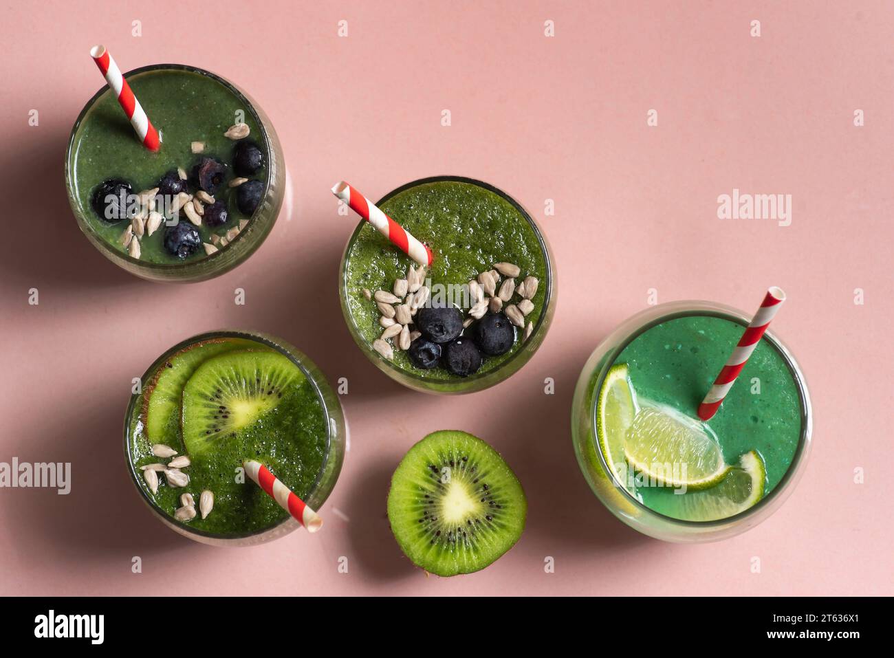 Frullato vegano verde con kiwi e lime in tazze di vetro con cannucce. Guarnita con mirtilli freschi e semi di girasole. Vista dall'alto dello sfondo rosa chiaro Foto Stock