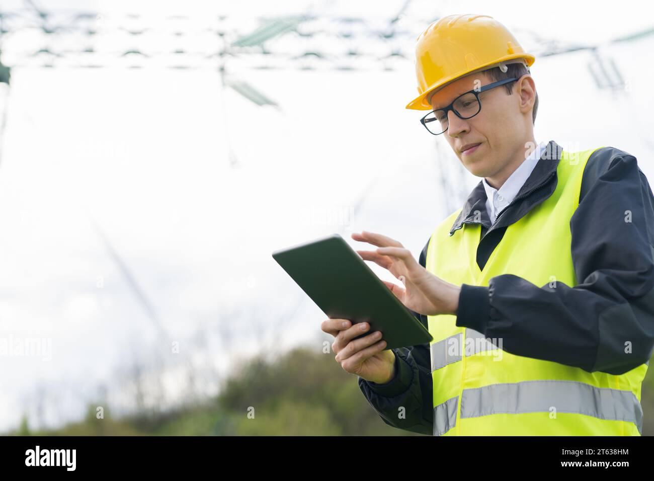 Progettare con un tablet digitale sullo sfondo di una torre della linea elettrica. Foto Stock