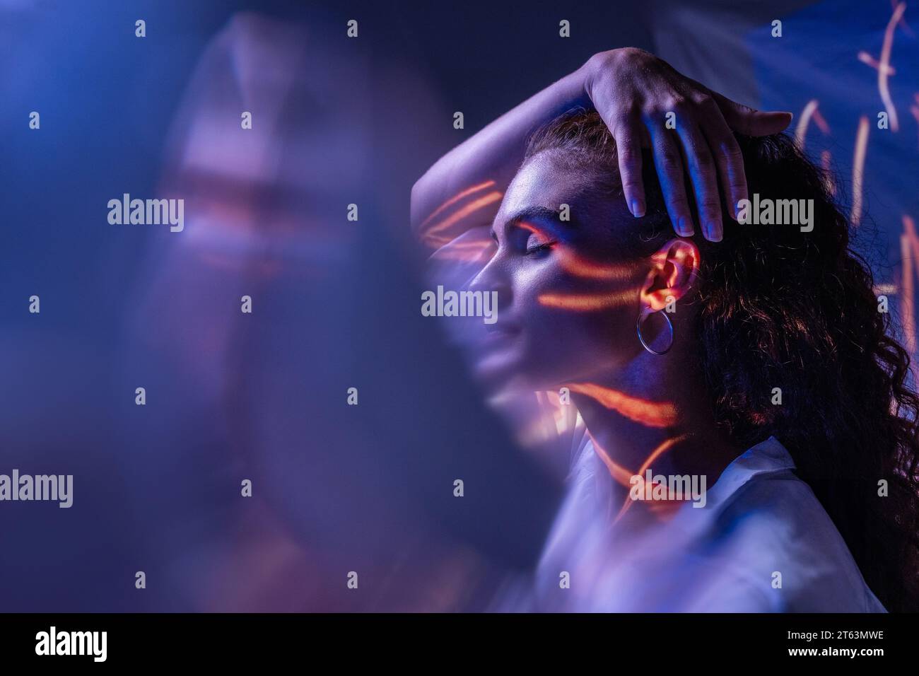 Avvolta da ombre e schemi di luce, una donna tocca la testa, simboleggiando l'intricata danza della spiritualità e degli stati mentali Foto Stock