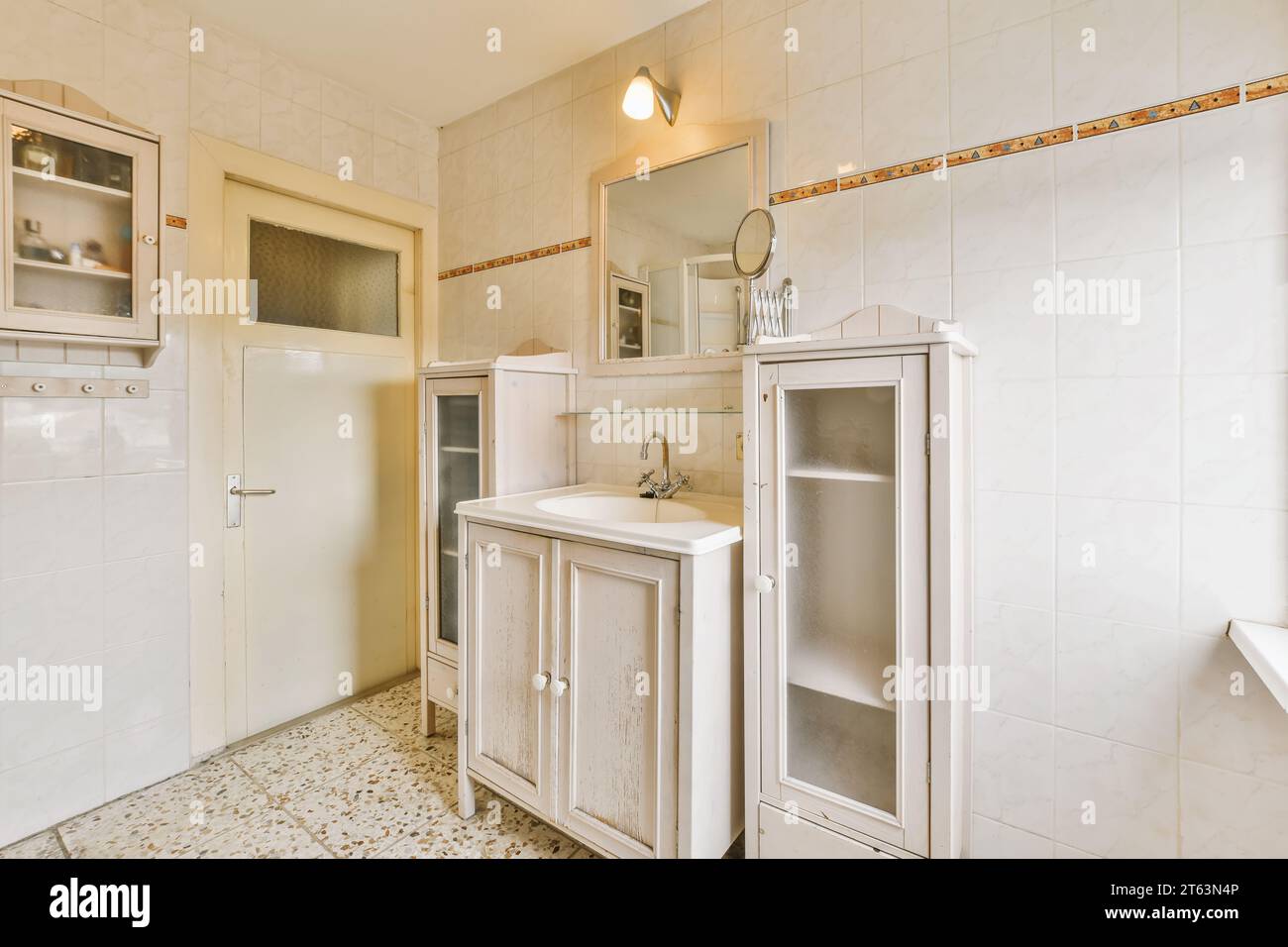 Specchio su lavabo d'epoca con armadi di legno vuoti in una cucina in stile country con pareti bianche a casa Foto Stock