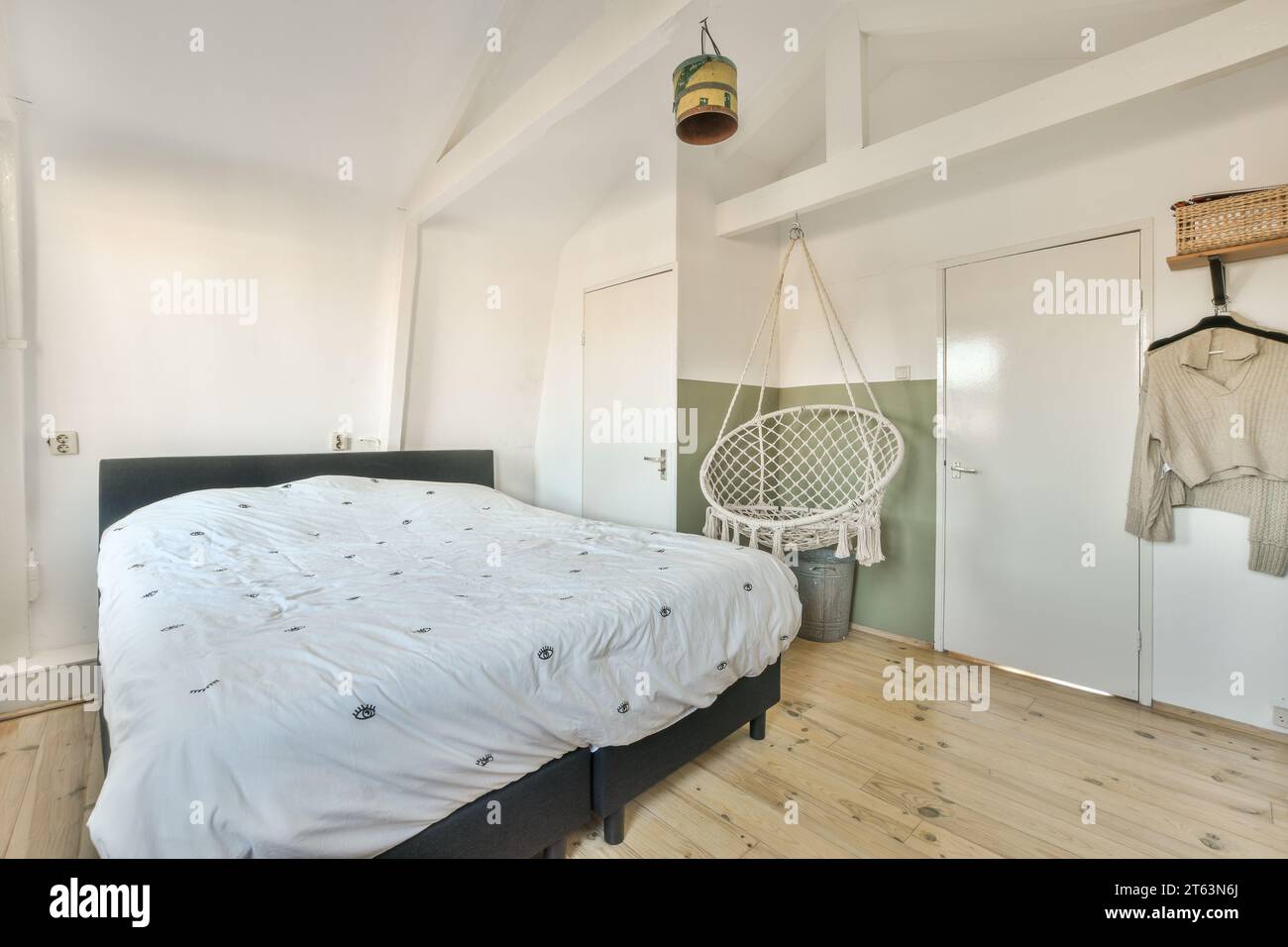 Comodo letto con sedia a dondolo e vestiti in una camera da letto contemporanea con pareti bianche e porte a casa Foto Stock