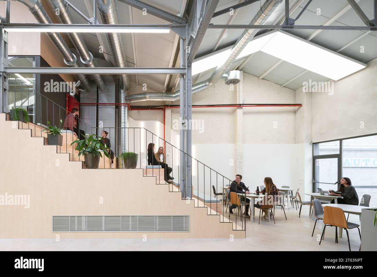 Spazioso ufficio di coworking a Madrid, Spagna, che presenta una miscela di design moderno con elementi industriali professionisti che lavorano e un laptop in primo piano Foto Stock