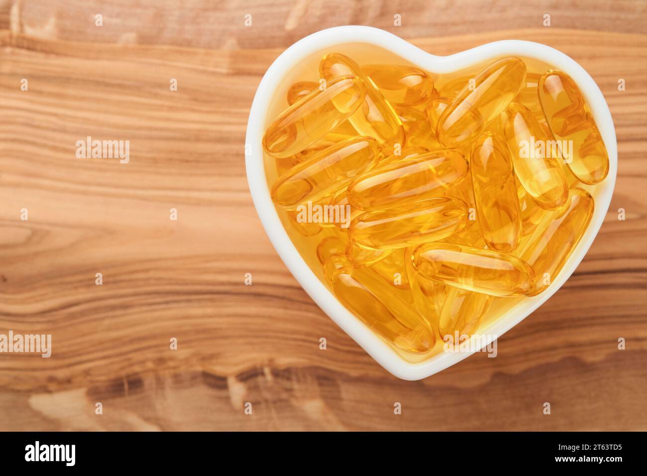 Capsule con vitamina D, e o acidi grassi Omega 3,6,9 in ciotola a forma di cuore su vecchi sfondi di legno. Olio di pesce riempito di olio per integratori alimentari. Supp. Naturale Foto Stock