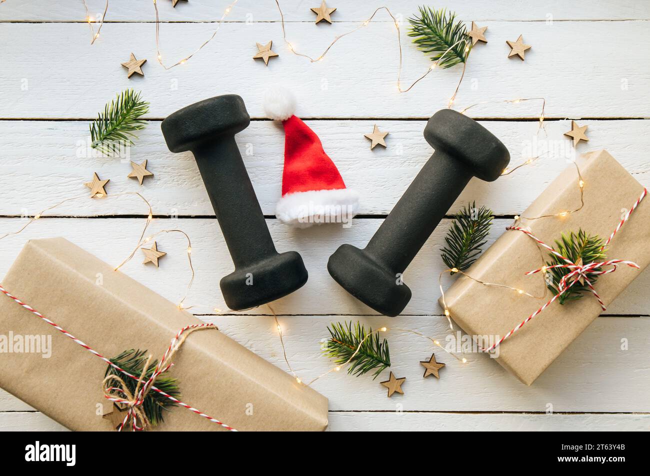 Stile di vita sano durante il periodo di festa di Natale concetto. Manubri neri con ornamenti natalizi su sfondo bianco in legno. Foto Stock