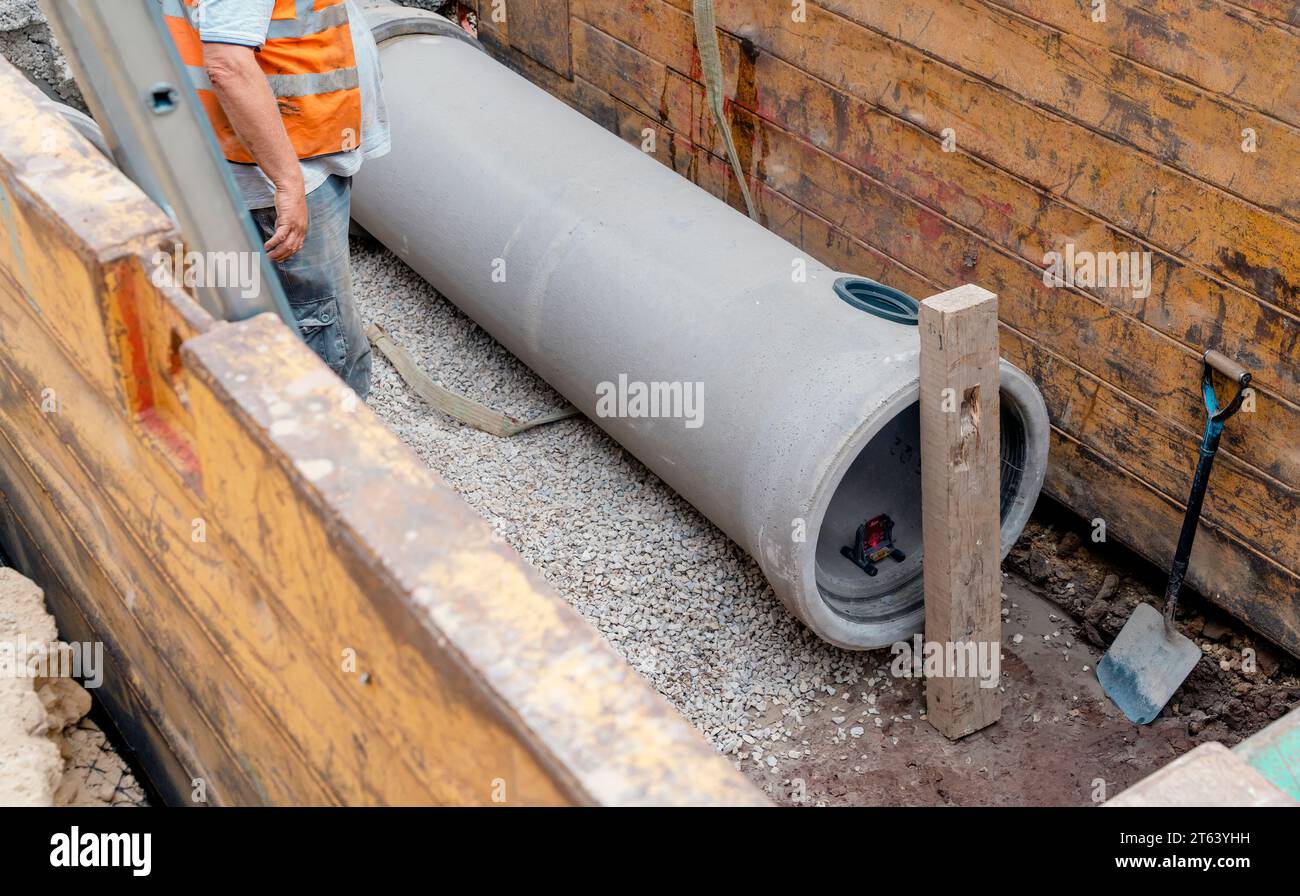 Costruttore installazione di un tubo di drenaggio in calcestruzzo di grande diametro protetto da un sistema di supporto per trincee durante lavori di drenaggio profondo Foto Stock