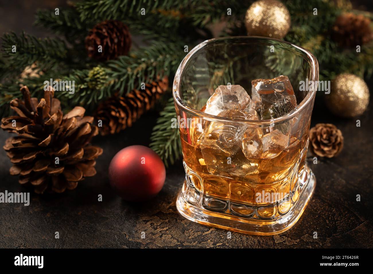 Bicchiere di whisky e ghiaccio su superficie di legno con decorazioni natalizie sullo sfondo Foto Stock