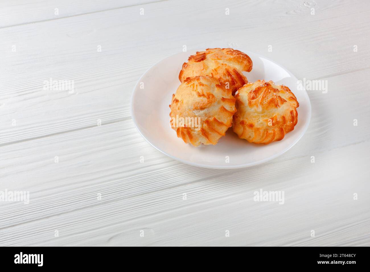 Profiterole dorate ripiene di panna, servite su un piatto bianco su un tavolo bianco. un delizioso abbinamento di dessert per ogni occasione. Foto Stock