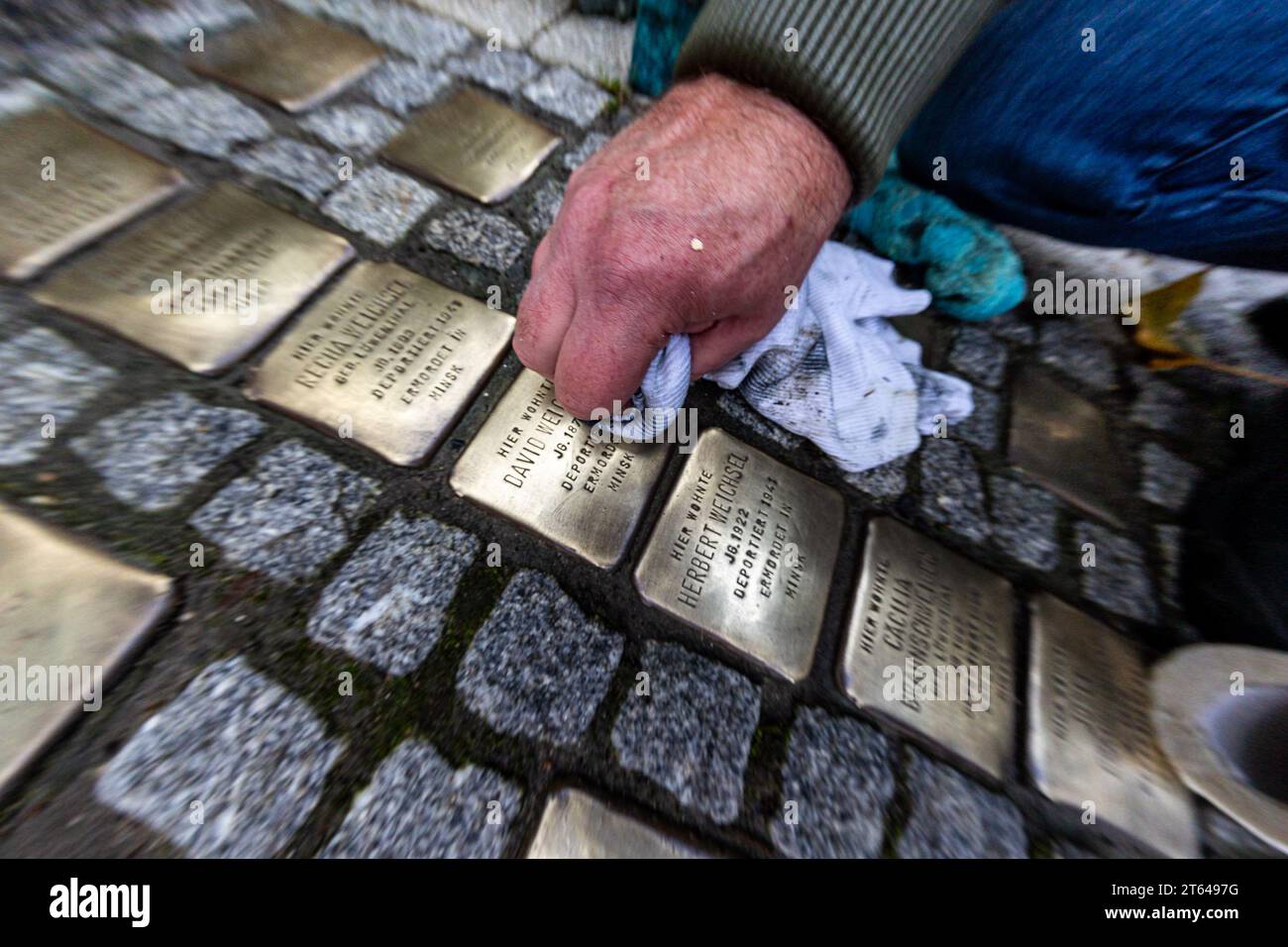 PRODUZIONE - 07 novembre 2023, Assia, Francoforte sul meno: Martin Dill lucida "Stolpersteine" (pietre inciampo) su un marciapiede a Francoforte, che commemora gli ebrei deportati durante l'era nazista. Nel frattempo, la Frankfurt Stumbling Stones Initiative ha chiesto la pulizia delle pietre commemorative. "La Stolpersteine di Francoforte dovrebbe brillare di nuovo il 9 novembre”, ha spiegato il coordinatore dell'iniziativa, Martin Dill. Tutti i comuni detergenti per metalli sono adatti per la pulizia delle lastre di ottone con i nomi e le date di vita delle vittime. Tuttavia, gli strumenti affilati, come le spazzole metalliche, dovrebbero Foto Stock