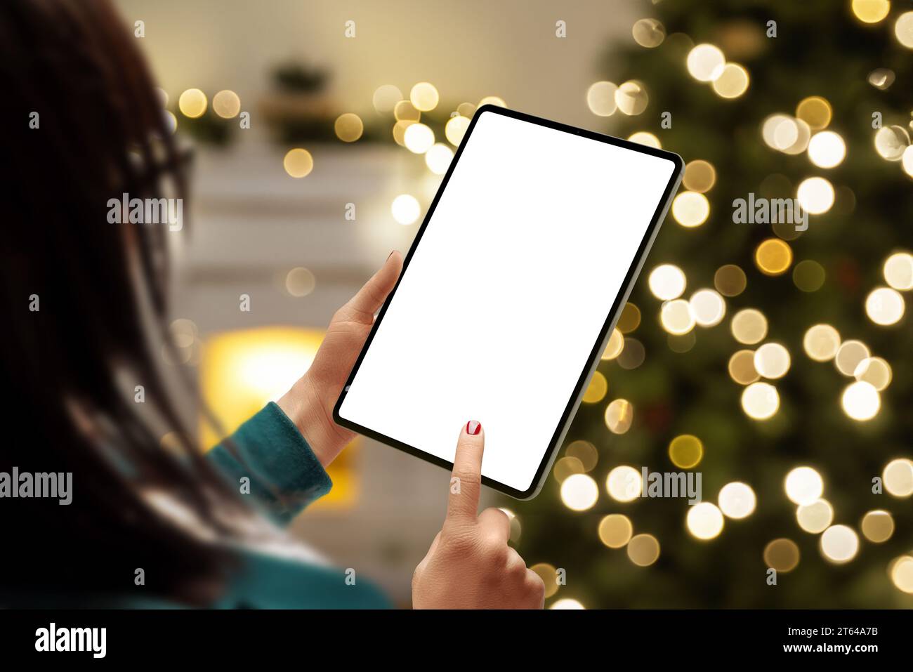 Donna con un modello tablet accanto a un albero di Natale, che offre uno schermo isolato per la presentazione di app o pagine Web. Ideale per mostrare app o web d Foto Stock