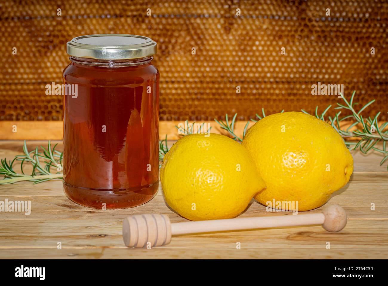 Vaso di miele, dispenser, rametto di rosmarino e due limoni su legno con un vero favo a nido d'ape sullo sfondo Foto Stock