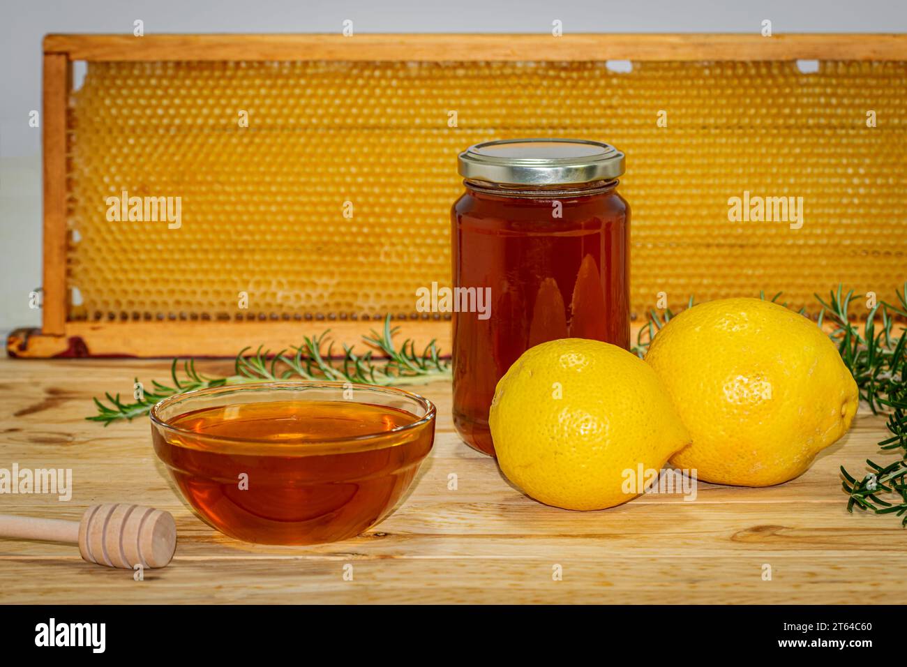 Vaso di miele, dispenser, recipiente con miele, rametto di rosmarino e due limoni su legno con un vero favo sullo sfondo Foto Stock