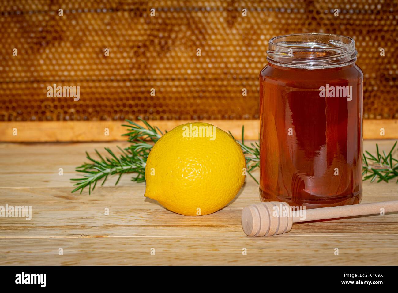 Vaso di miele senza coperchio, dispenser, rametto di rosmarino e limone su legno con un vero favo a nido d'ape sullo sfondo Foto Stock