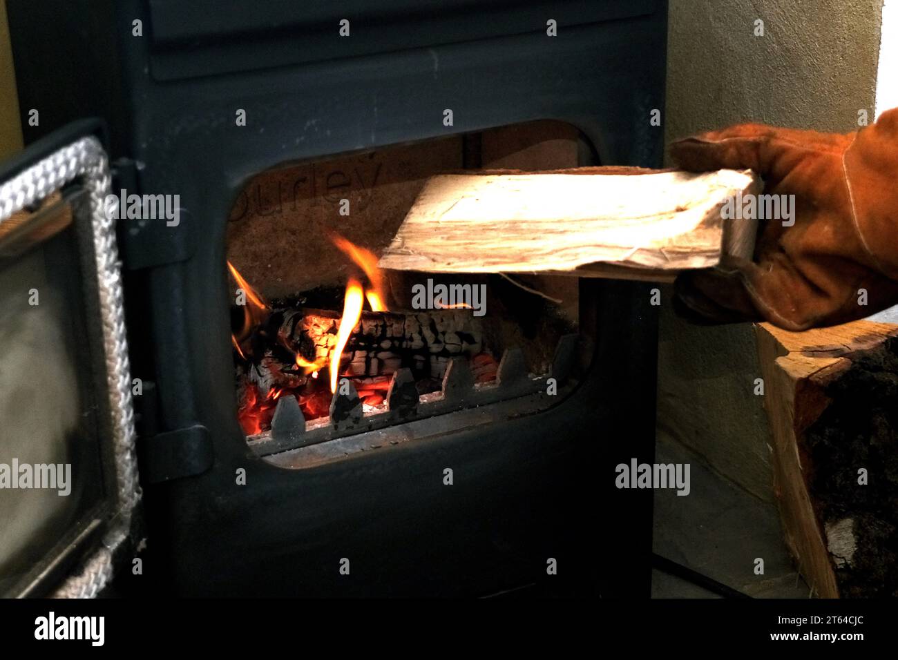 Guanti a mano con l'aggiunta di un tronco di legno in una stufa a legna, uk Nov 2023 Foto Stock