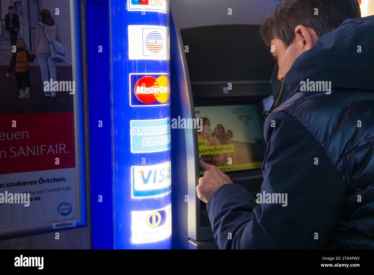 Uomo in un bancomat internazionale a Heidelberg, Germania (modello rilasciato). Sul display viene visualizzato BARGELD GEDRUCKTE FREIHEIT (libertà stampata in contanti) Foto Stock