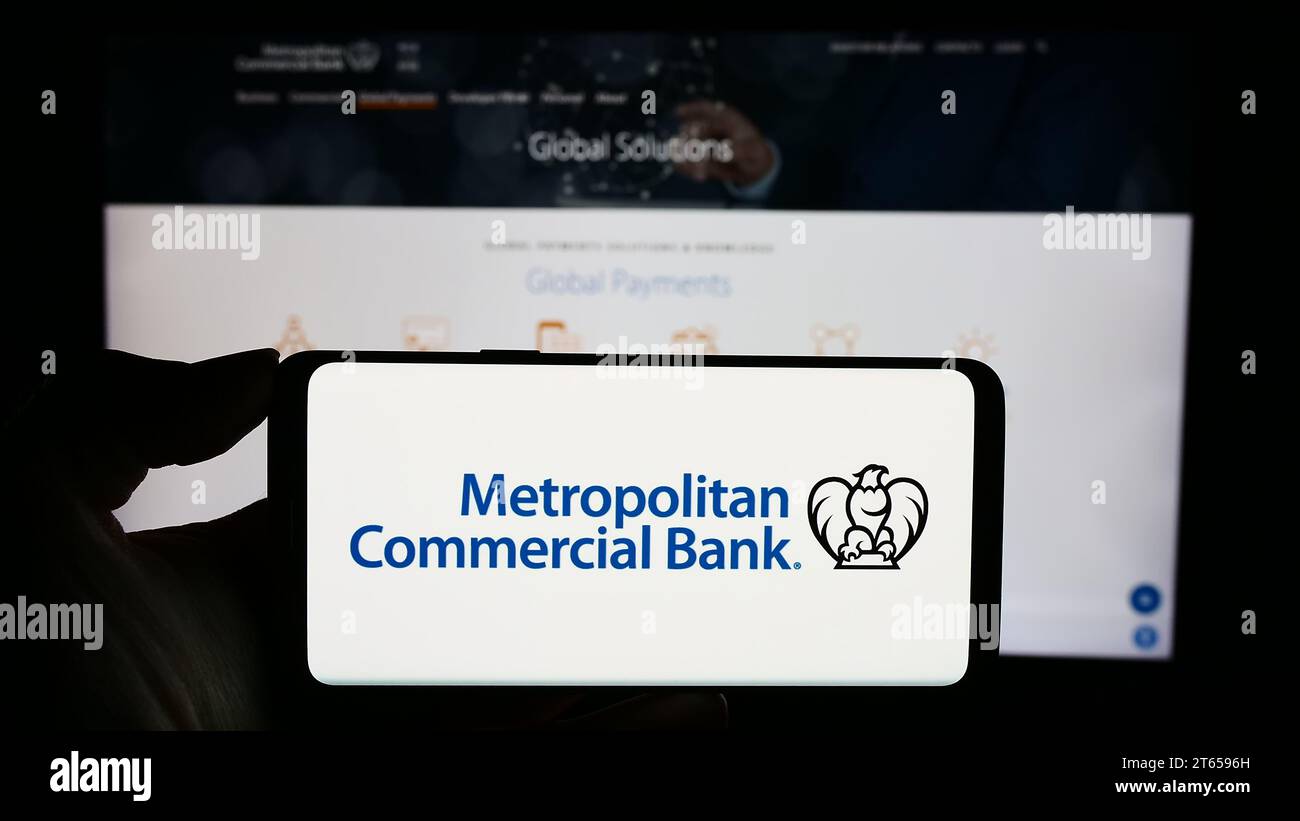 Persona in possesso di un cellulare con il logo della società finanziaria statunitense Metropolitan Commercial Bank (MCB) davanti alla pagina Web. Concentrarsi sul display del telefono. Foto Stock