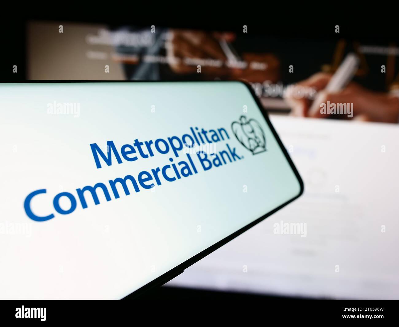 Telefono cellulare con logo della società finanziaria statunitense Metropolitan Commercial Bank (MCB) davanti al sito Web. Mettere a fuoco il display centrale sinistro del telefono. Foto Stock