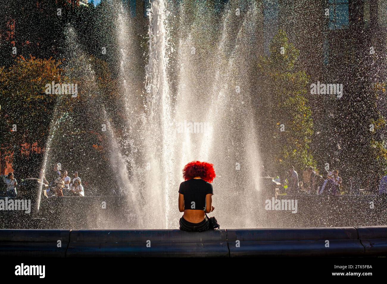 Una giovane donna nera con i capelli rossi seduta vicino alla fontana a Washington Square Park, Manhattan, New York City Foto Stock