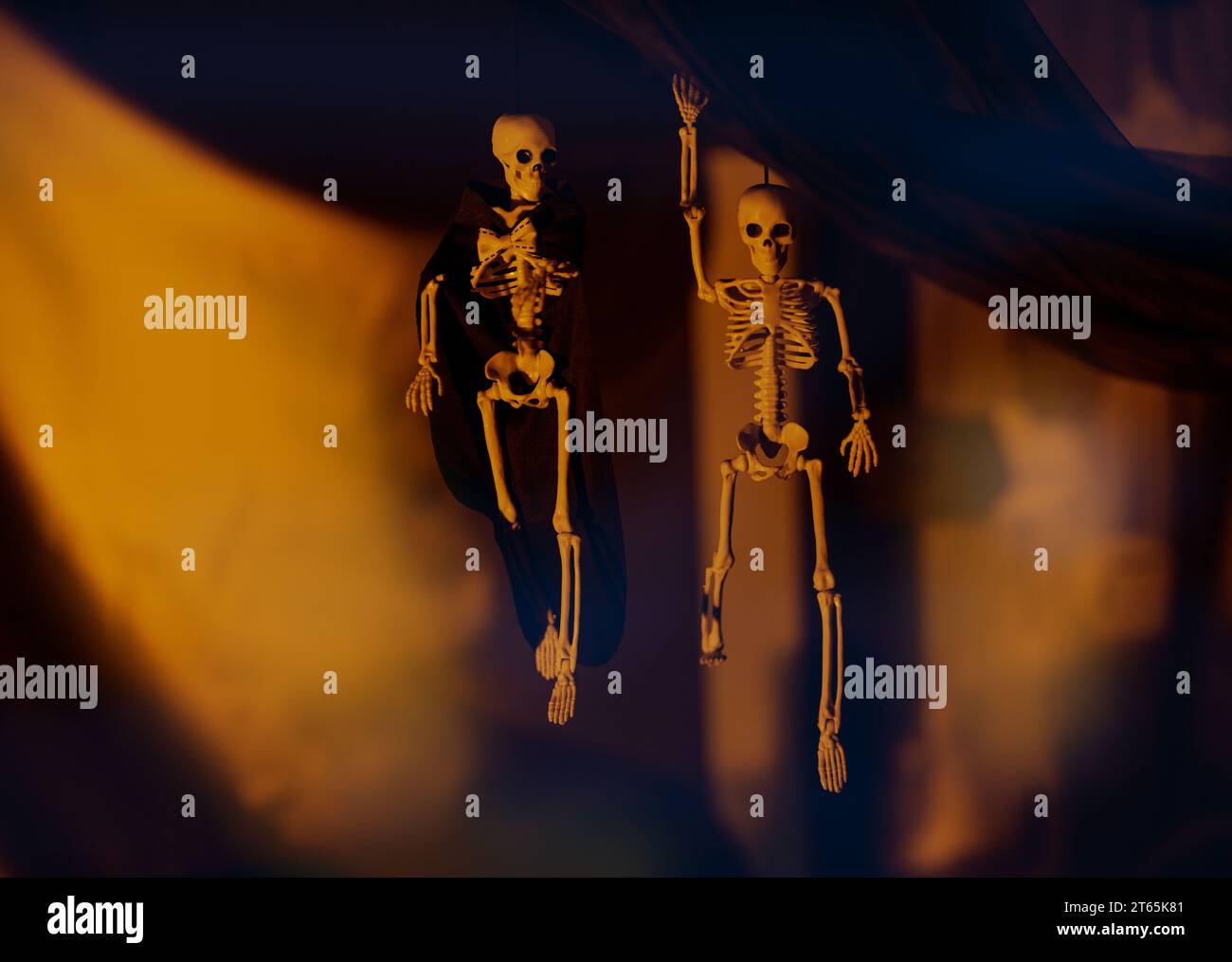 Decorazione per la festa di Halloween. Due scheletri spettrali appesi al panno nero su sfondo giallo in una stanza buia. Foto Stock
