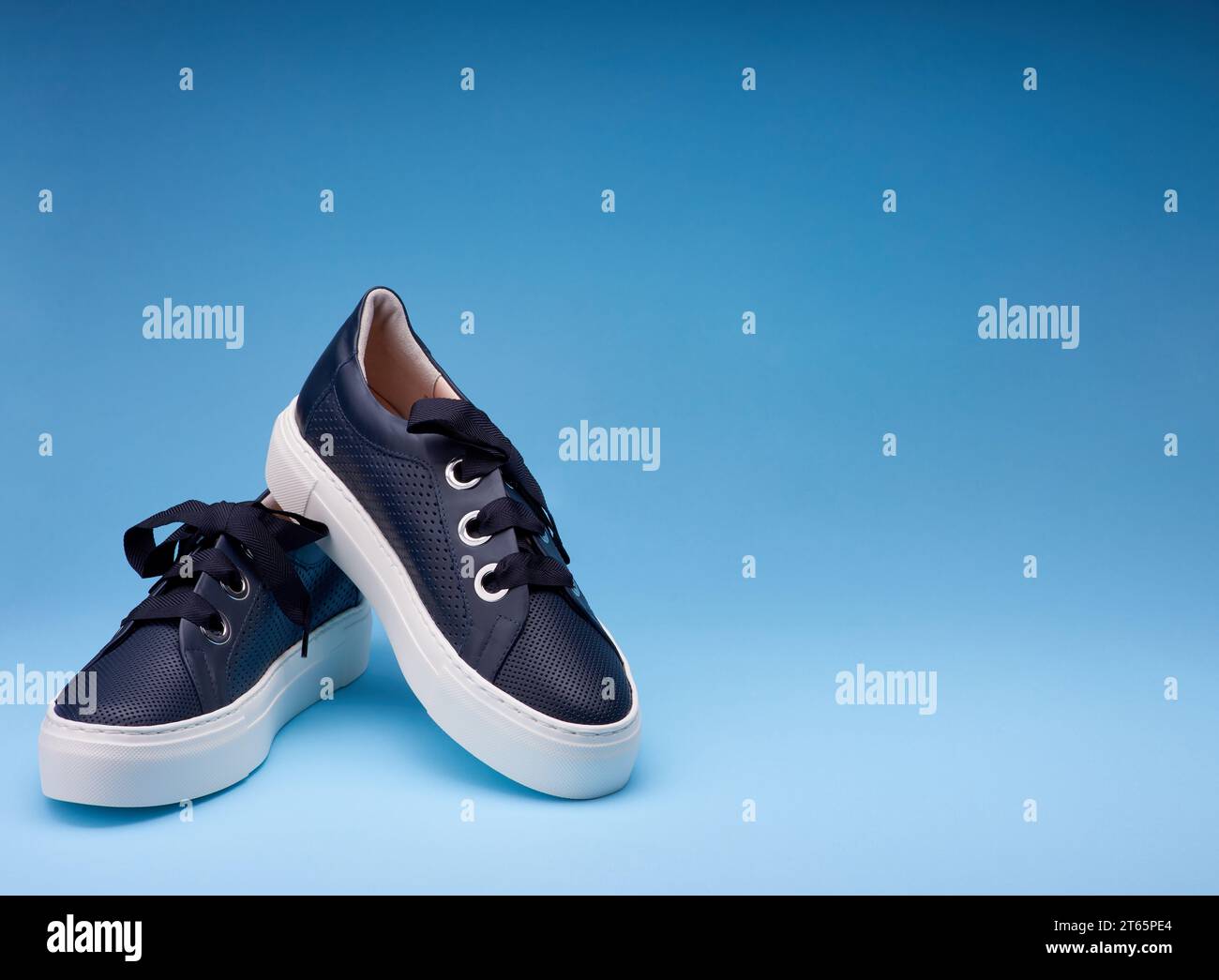 Un paio di sneaker in pelle traforata blu navy con spessa placca bianca e spessa lacca isolata sullo sfondo sfumato blu con spazio copia f Foto Stock
