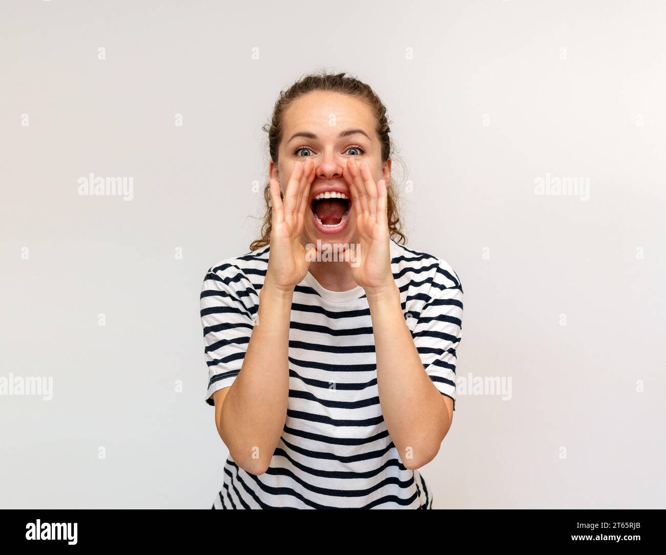 La donna che indossa una t-shirt a righe grida ad alta voce cogliendo le mani intorno alla bocca. Urla e grida. Foto Stock