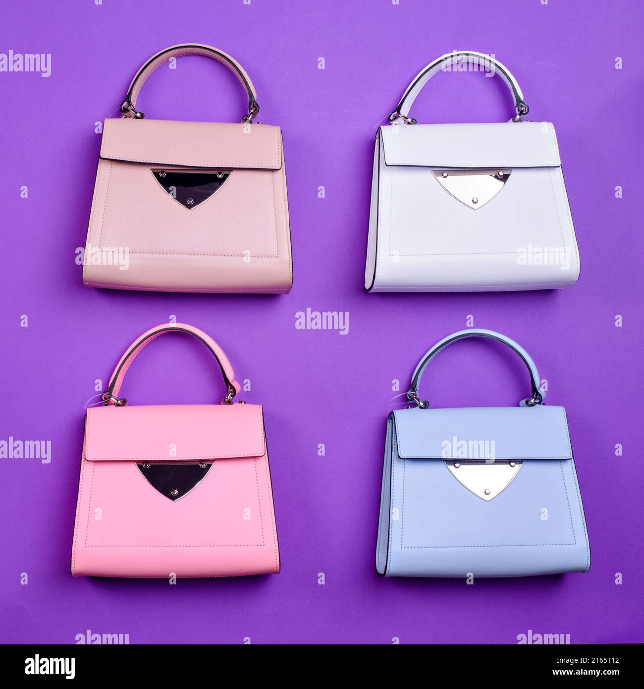 Modello piatto di quattro eleganti borse in pelle con manico superiore da donna dello stesso design ma con colori diversi su sfondo viola. Blog o rivista di moda. Choo Foto Stock
