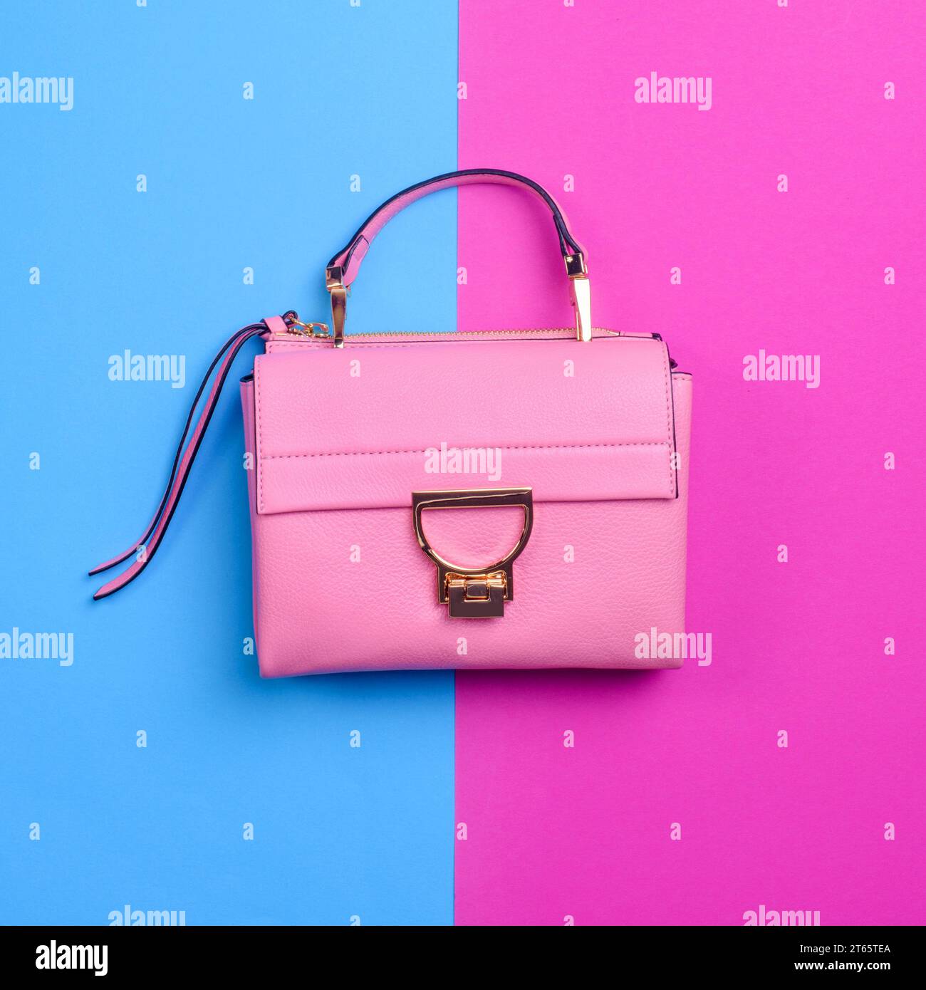 Elegante borsa da donna in pelle rosa con finiture nere, dettagli in metallo dorato, manico superiore e cerniera isolata su uno sfondo blu vivace e fucsia. Foto Stock