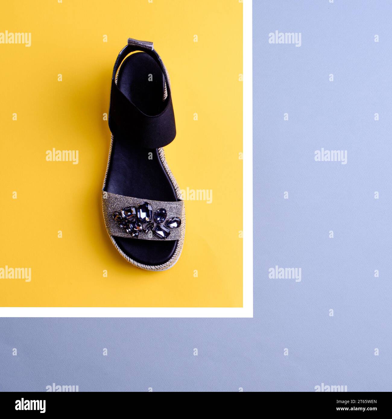 Elegante sandalo nero-argento decorato con strass su sfondo giallo e grigio. Blog di moda. Sconto, saldi stagionali. Calzature r Foto Stock