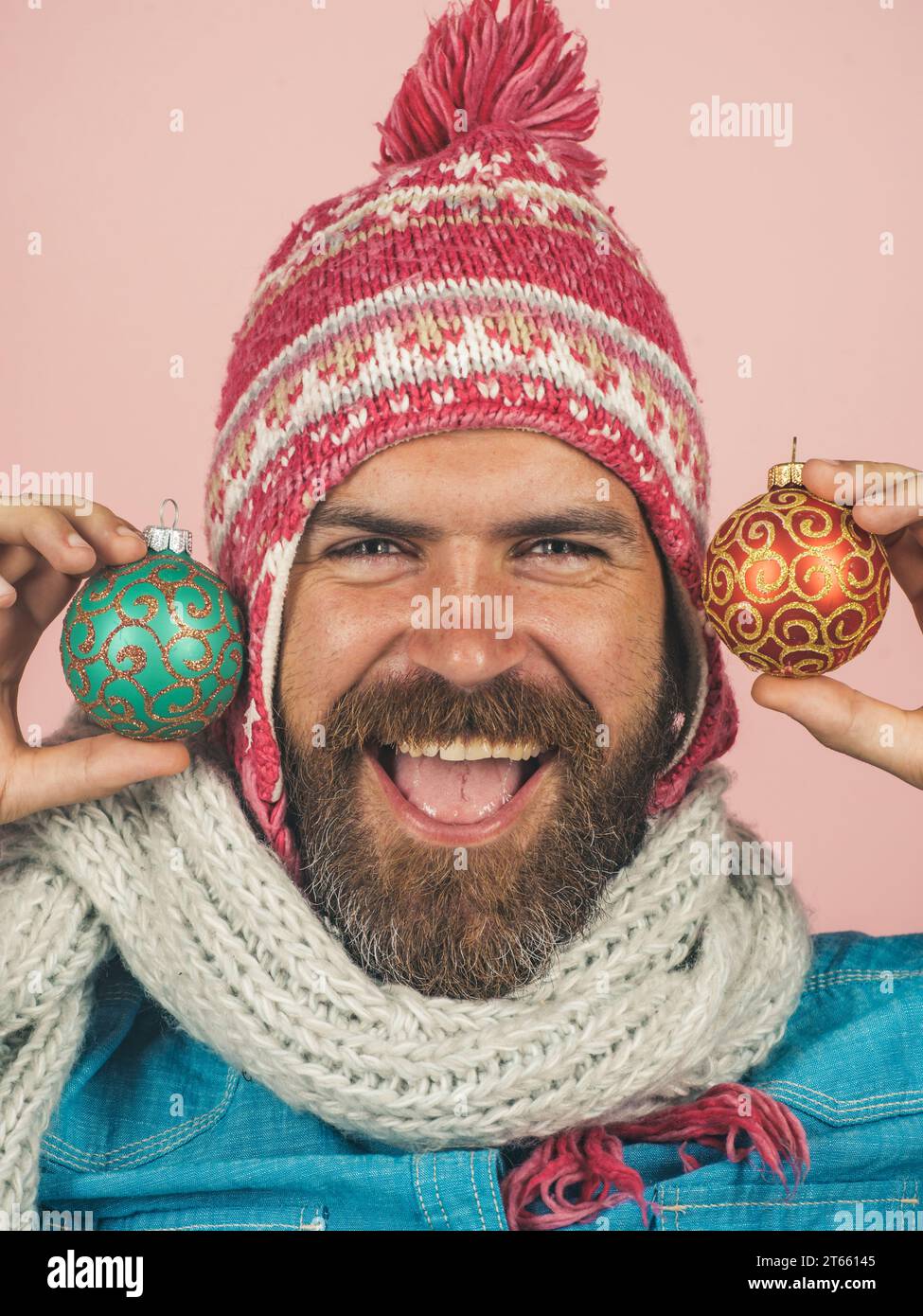 Uomo barbuto con palle decorative per decorare l'abete di Capodanno. Un ragazzo felice con cappello e sciarpa con palline multicolori per alberi di Natale. Natale Foto Stock