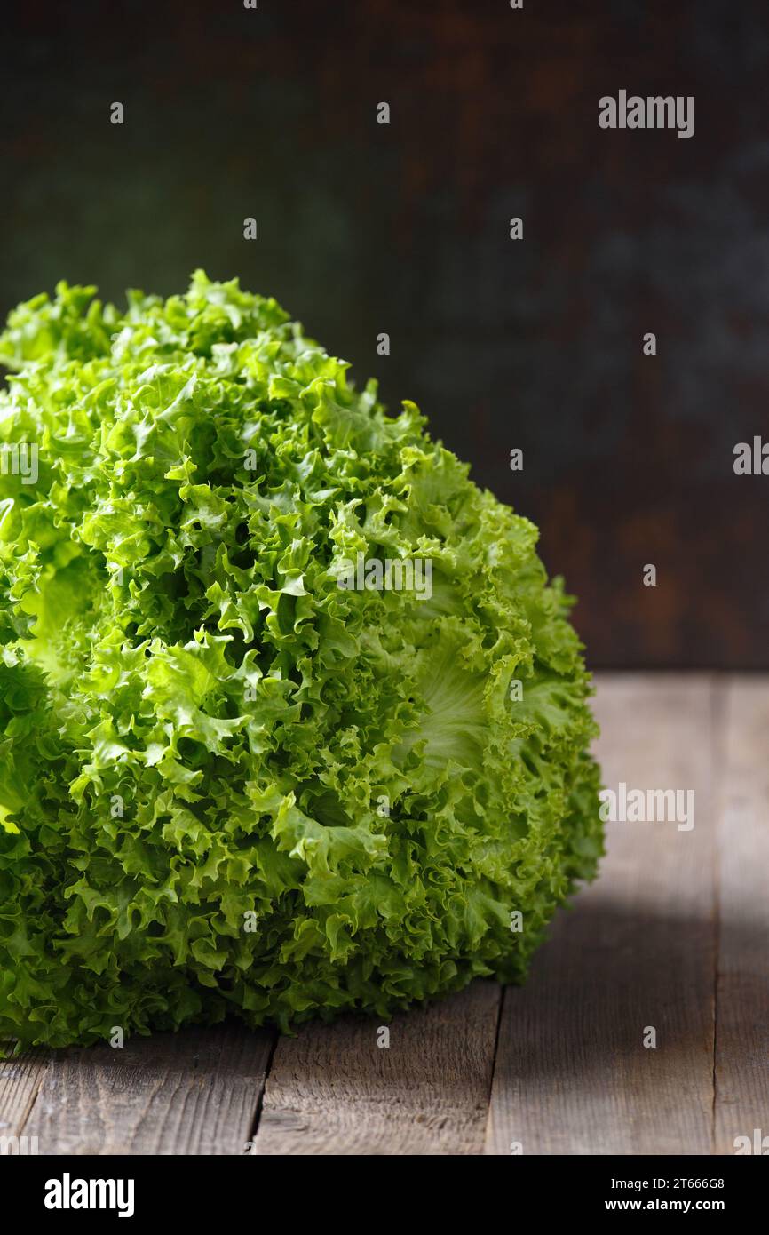 Un grande mazzo di foglie di lattuga verde fresca su un tavolo di legno e uno sfondo scuro. Cibo sano, fonte di minerali e vitamine. Foto Stock