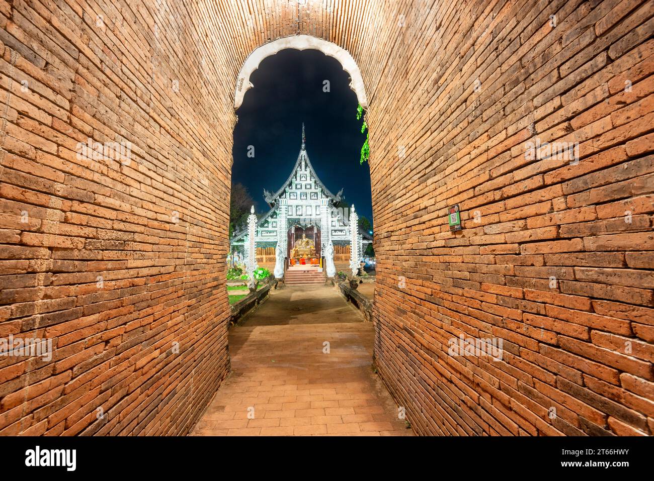 Alto, stretto, ad arco, corto tunnel, fiancheggiato da mattoni rossi, che conduce verso la porta di ingresso di ornati, tempio costruito in legno di teak, con facciata decorativa in argento e. Foto Stock