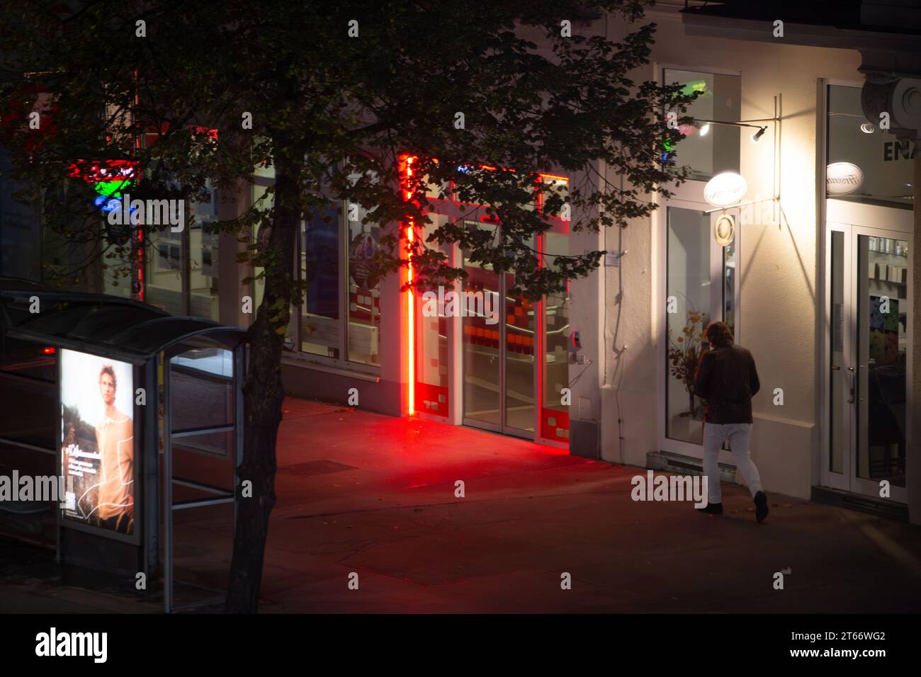 Un uomo in abiti invernali cammina sul marciapiede sullo sfondo delle luci rosse della città di notte in inverno, Vienna Austria Foto Stock