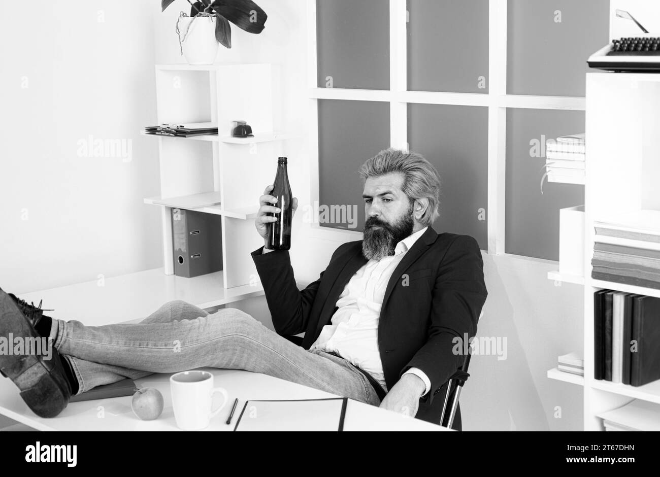 Fine della giornata lavorativa. Un giovane dipendente d'affari che beve in ufficio alla scrivania. Foto Stock