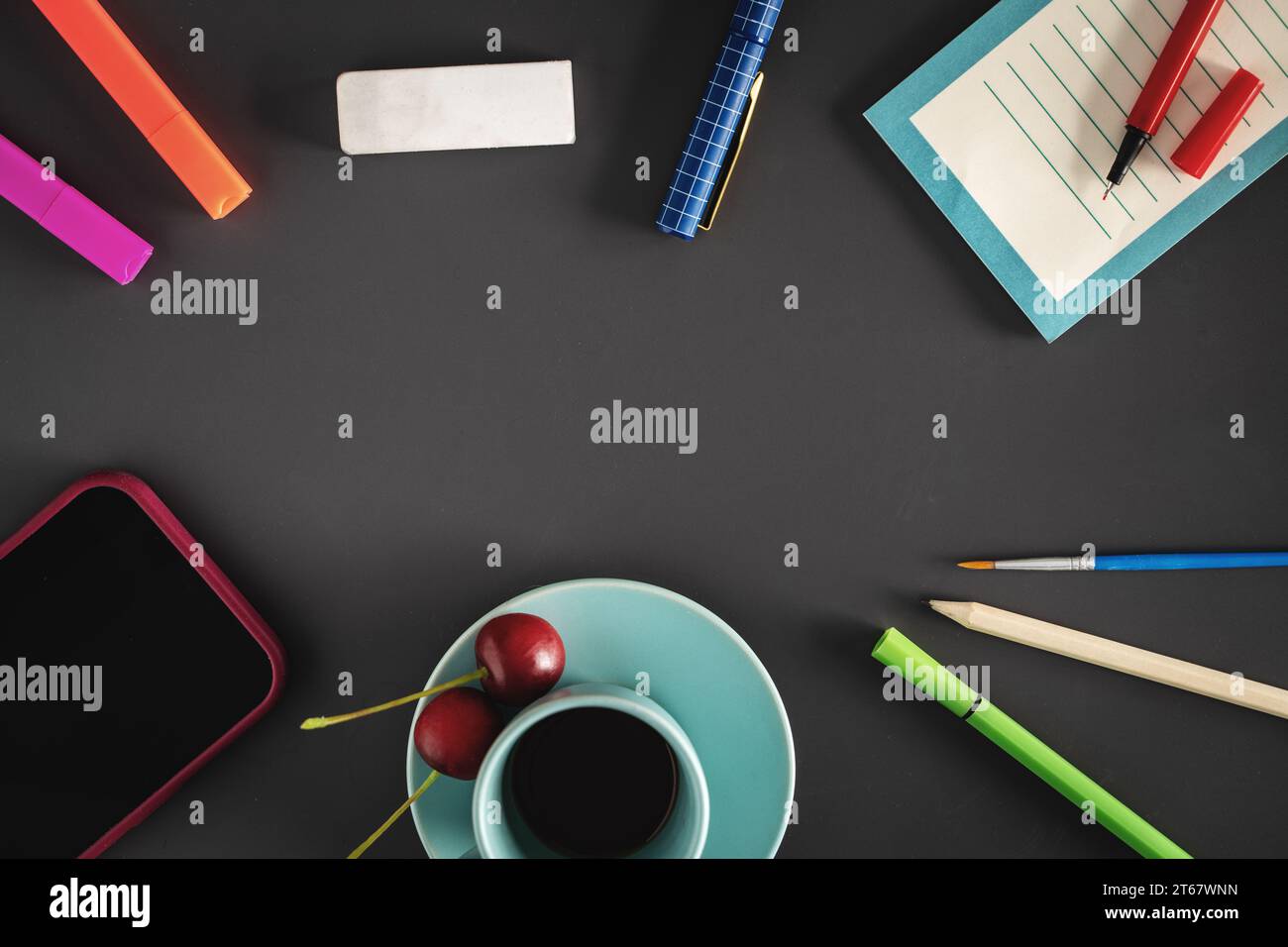 Vista dall'alto di uno spazio di lavoro elegante e ordinato con caffè, ciliegie fresche, cancelleria e uno smartphone su una superficie scura con spazio per le copie nel cente Foto Stock