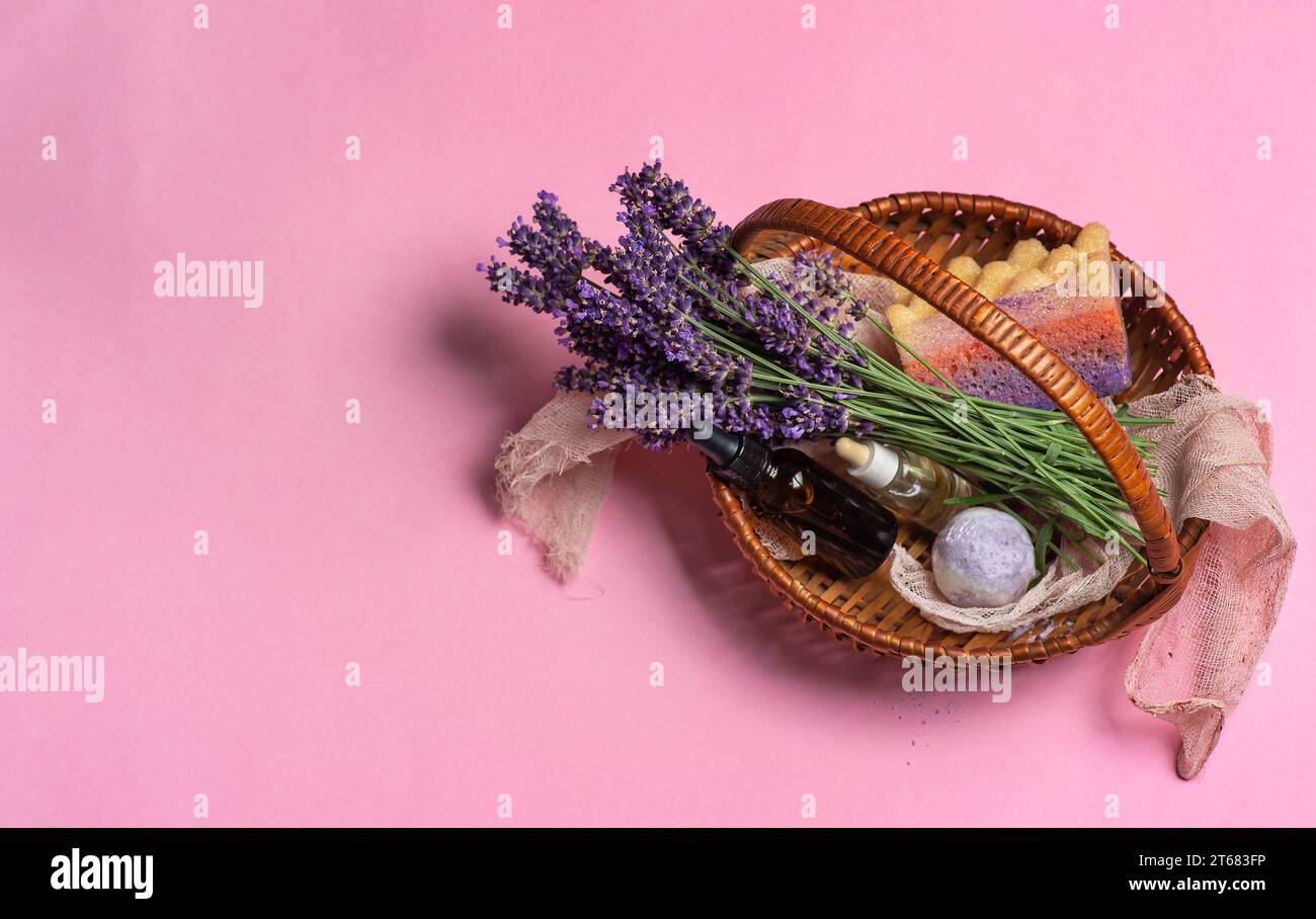 Fiori di lavanda freschi, olio essenziale in bottiglia, sale da bagno alla lavanda e spugna da bagno in un piccolo cestino di vimini su sfondo rosa pastello. Con la copia S Foto Stock