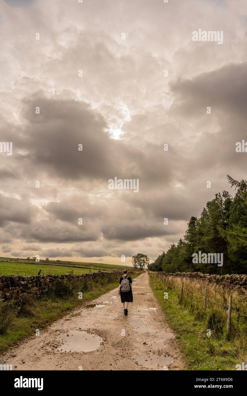 Ragazza vestita e zaino che si allontana dalla macchina fotografica lungo una pista umida e fangosa a Osmotherly, North Yorkshire, Inghilterra, Regno Unito Foto Stock