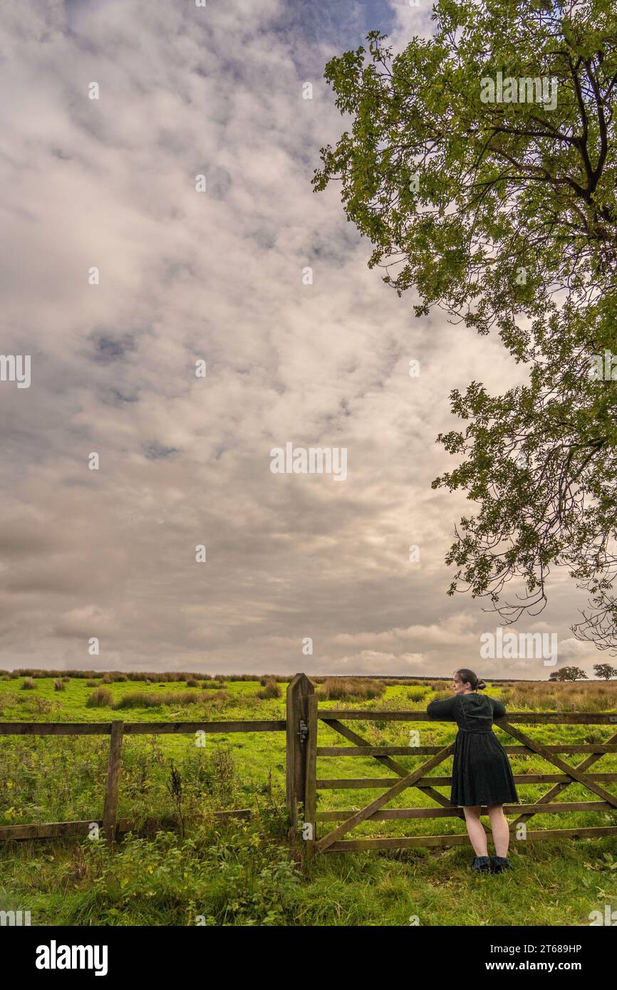 La ragazza si appoggiava contro il cancello a 5 bar per contemplare la vita in campagna a Osmotherly, North Yorkshire, Inghilterra, Regno Unito Foto Stock