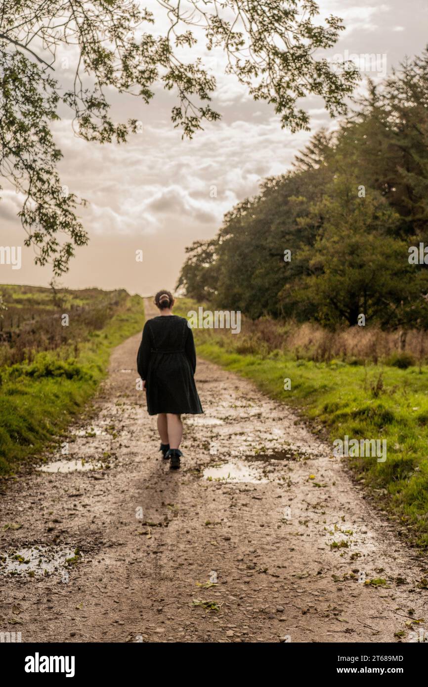 Ragazza vestita che si allontana dalla macchina fotografica lungo una pista umida e fangosa a Osmotherly, North Yorkshire, Inghilterra, Regno Unito Foto Stock