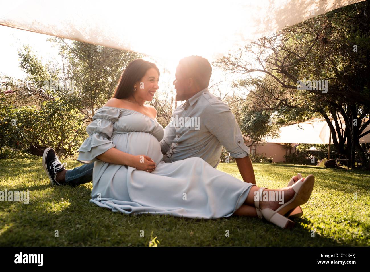 Una donna latina incinta e una coppia di uomini africani seduti in un lussureggiante parco illuminato dal sole Foto Stock