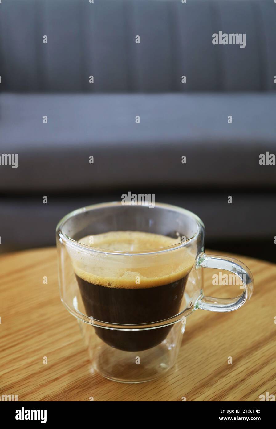 Tazza di caffè caldo in una tazza trasparente con un divano sfocato sullo sfondo Foto Stock