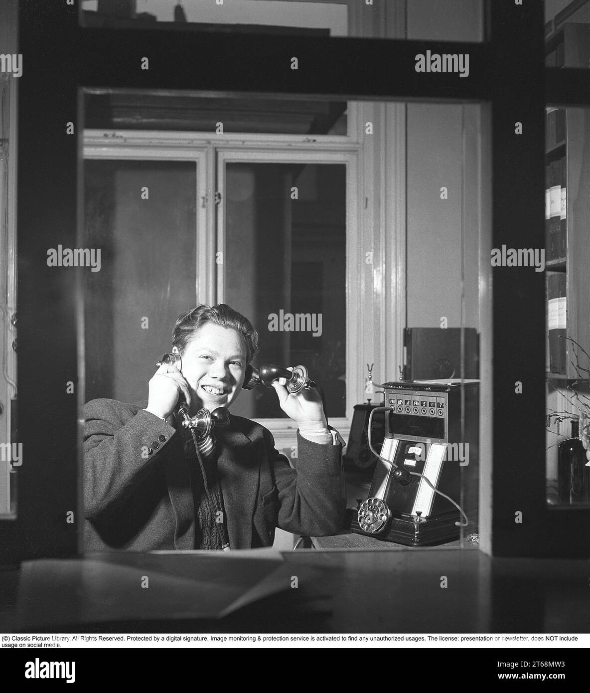 La telefonia negli anni '1940 Un uomo a un centralino telefonico. Collega le chiamate in entrata e in uscita alla persona giusta utilizzando i cavi per i rispettivi telefoni in un centralino telefonico. Sembra felice di essere al lavoro, sorridendo a parlare su due telefoni contemporaneamente. Svezia 1945 Kristoffersson rif O149-3 Foto Stock