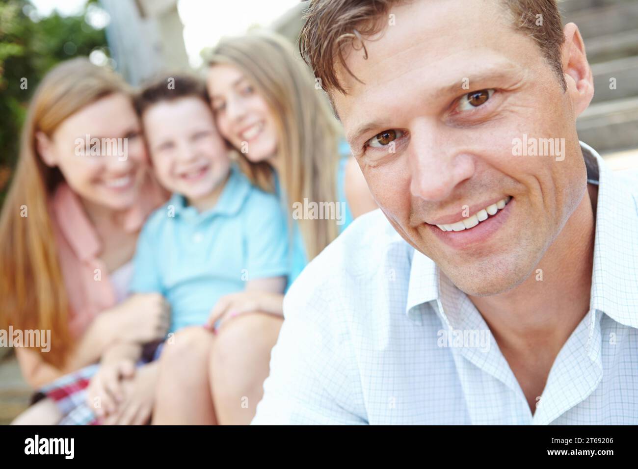 Ritratto di una famiglia perfetta. Bel padre con una famiglia seduta dietro di lui mentre è all'aperto. Foto Stock