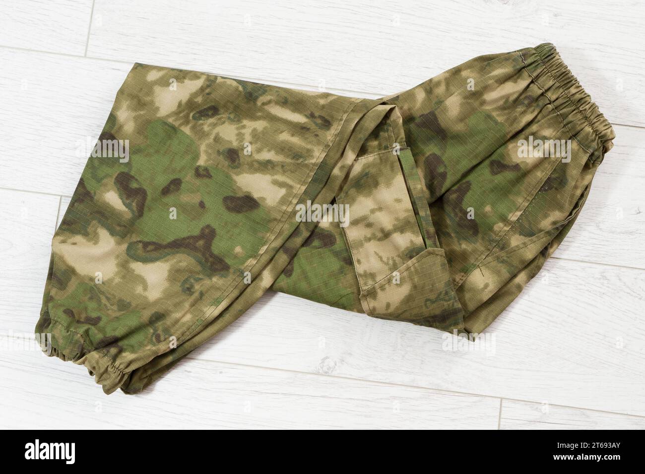 Pantaloni camouflage con primo piano su sfondo in legno, pantaloni kaki verdi. Pantaloni elastici da soldato camouflage su sfondo in legno. Foto Stock
