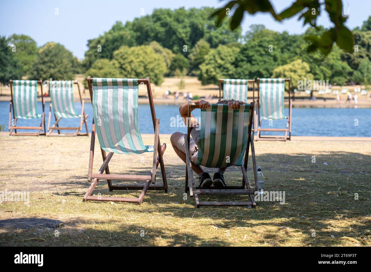 Un uomo si rilassa su una sdraio all'ombra di un albero in una calda giornata estiva in un parco pubblico Foto Stock