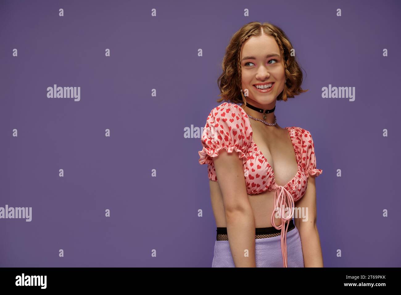 giovane donna felice in cima corta con cuori sorridenti su sfondo viola, emozione positiva Foto Stock