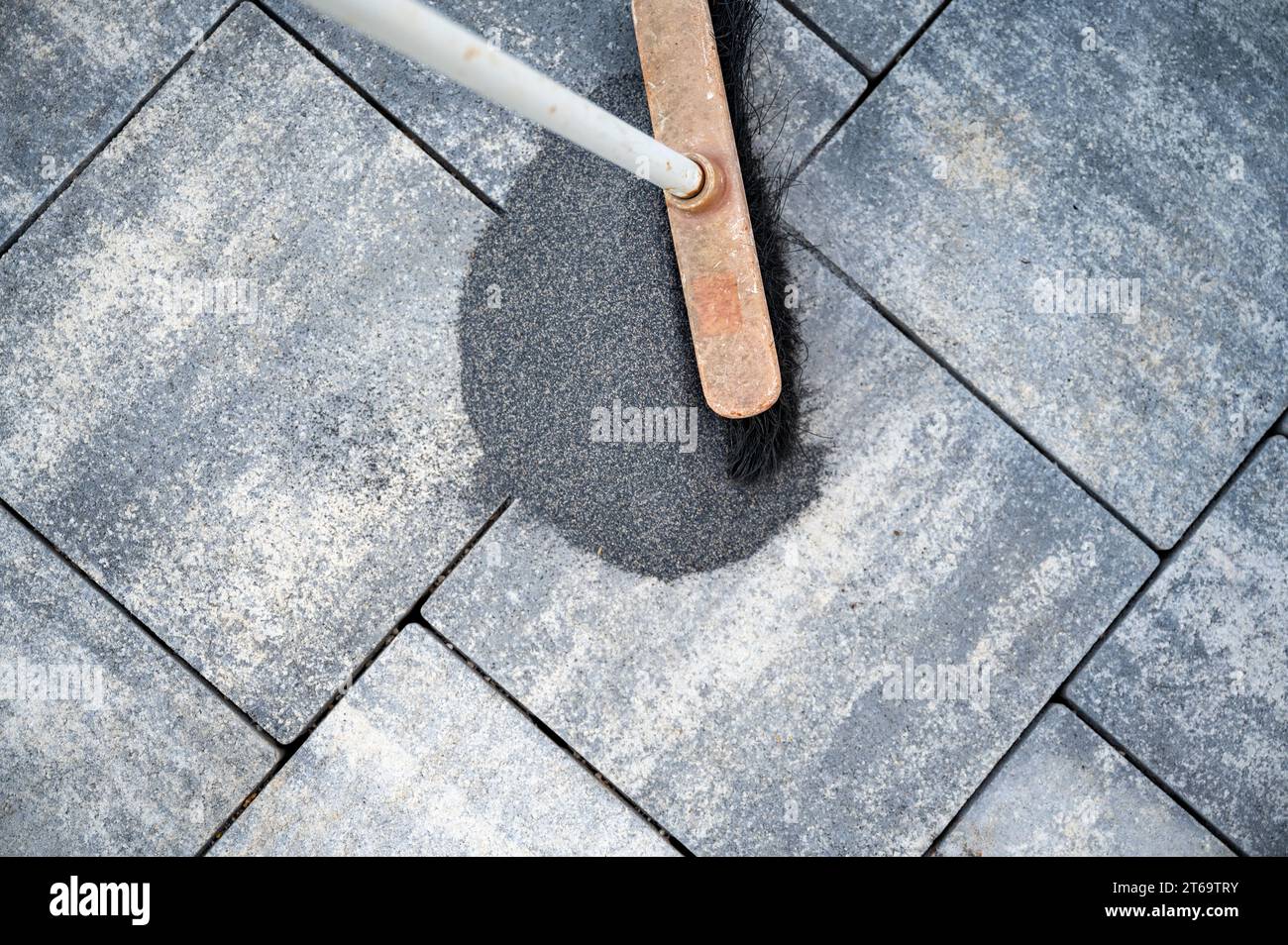 Vista dall'alto di una scopa spazzolando una lacuna di piastrelle tra gli spazi del marciapiede appena pavimentato o del patio con piastrelle di cemento grigie. Foto Stock